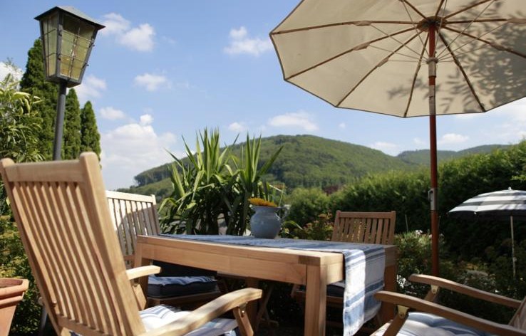 Sonnige Terrasse im Haus Feuchtl mit Sonnenschirm, Holzmöbeln und weitem Blick in die Hügel des Wienerwaldes
